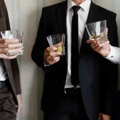 Uomini eleganti con bicchieri di whisky, perfetti per un dress code cocktail.