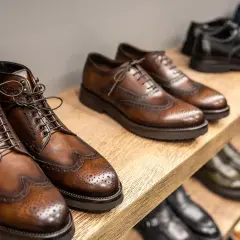 Vari tipi di scarpe eleganti in pelle marrone e nera, con dettagli traforati, disposte su scaffali di legno.