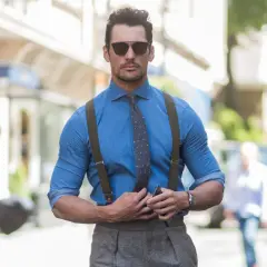 Uomo magro con camicia blu, cravatta e bretelle, occhiali da sole, in strada.