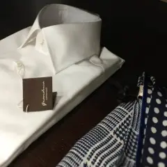 Camicia bianca da uomo con abbottonatura maschile impeccabile, accanto a un fazzoletto da taschino a pois e a quadretti.