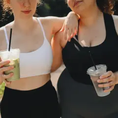 Due amiche con fianchi a violino si godono una bevanda fresca dopo l'allenamento, una con un matcha, l'altra con acqua.