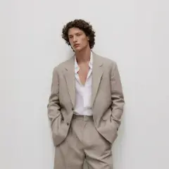 Uomo con giacca beige e camicia bianca sbottonata: un'idea di cosa mettere sotto la giacca uomo per un look casual-chic.