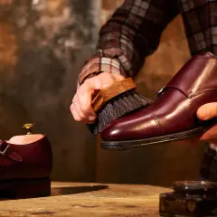 Un uomo lucida scarpe in pelle bordeaux con una spazzola, un rituale per mantenerle splendenti.