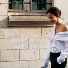 Donna con camicia bianca oversize e pantaloni neri, un look smart casual con una collana dorata.