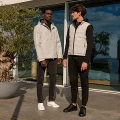 Due uomini con un outfit uomo elegante sportivo, uno con giacca grigia e jeans, l'altro con gilet grigio e pantaloni neri, in piedi all'esterno.