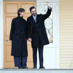 Una coppia, lui saluta, si tiene per mano davanti a una porta. Un'atmosfera da rama duwaji.