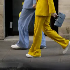 Un outfit tailleur con sneakers, giallo vivace e azzurro pastello, camminano sul marciapiede.