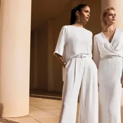 Due donne eleganti in bianco, un'ispirazione su come vestirsi ad un matrimonio con pantaloni ampi o abito longuette.