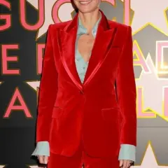 Gwyneth Paltrow in un completo rosso di velluto, sorride davanti a uno sfondo con stelle e lettere rosa e oro.