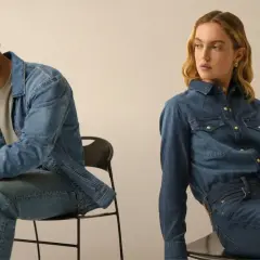 Coppia in total look denim. Lui con giacca e jeans, lei con camicia e jeans, entrambi con un fit che si stringe verso il basso, il tapered fit significato.