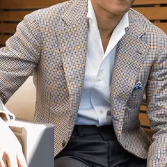 Uomo con giacca a quadri marrone, blu e arancione, camicia bianca e fazzoletto blu. Collezione drop 4.