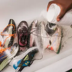 Mani versano polvere da un contenitore su diverse scarpe da ginnastica in una vasca da bagno, un modo per disinfettare scarpe usate.