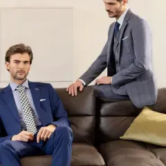 Due uomini eleganti in lounge suit siedono su un divano di pelle marrone. Uno è blu, l'altro grigio a quadri.