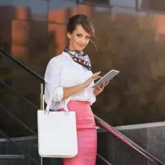 Donna con gonna a tubino rosa, camicia bianca e foulard colorato, tiene un tablet. Le scarpe per gonna a tubino perfette per questo look.