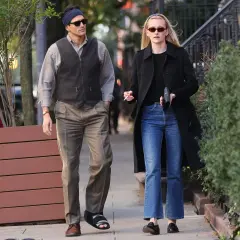 Coppia passeggia, lui con gilet e fascia, lei con cappotto e jeans a zampa. Un look che ricorda lo stile di Calvin Klein stilista.