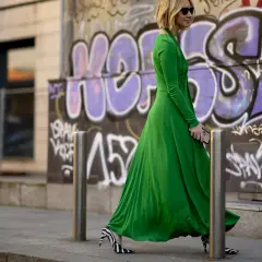 Donna con vestito lungo elegante verde smeraldo e scarpe zebrate, cammina con passo deciso davanti a un muro con graffiti.