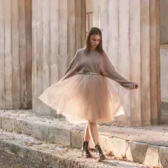 Ragazza con un outfit gonna tulle lunga color cipria, maglione oversize e anfibi, passeggia tra colonne antiche.