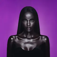 Anok Yai, con pelle lucida e capelli neri, posa con uno sguardo intenso su sfondo viola.