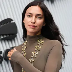 Irina Shayk, con un look audace e una collana d'oro, posa davanti a un logo.