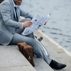Uomo in vestito grigio legge il giornale, con scarpe nere eleganti. Un dilemma: vestito grigio che scarpe abbinare?