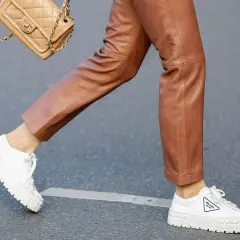 Un outfit chic con pantaloni in pelle marrone e sneakers bianche donna Prada. Una borsa Chanel completa il look.