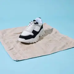 Sneaker bianco e nero su asciugamano beige, un metodo per asciugare scarpe bagnate dentro.