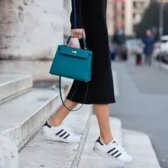 Scarpe da ginnastica bianche con strisce nere abbinate a un tubino nero e una borsa turchese.