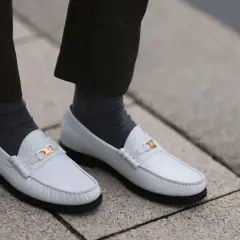 Scarpe pulite bianche con fibbia dorata, calzini grigi e pantaloni scuri.
