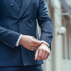 Uomo che sistema il polsino della sua giacca blu, un perfetto abbinamento giacca blu uomo per un look elegante.