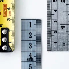 Tre metri diversi mostrano come si misura il tacco di una scarpa: uno giallo con indicazioni in pollici e centimetri, uno azzurro con numeri grandi e uno metallico con tacche precise.