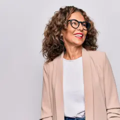 Donna sorridente con occhiali e blazer beige, un esempio di come vestirsi a 50 anni con stile.
