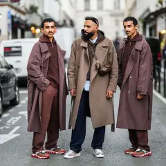 Tre uomini con eleganti stili abbigliamento uomo, cappotti lunghi e pantaloni coordinati, posano in strada.