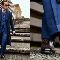 Uomo con outfit old money: completo blu a quadri, cappotto lungo, cravatta e scarpe stringate marroni.