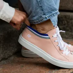 Mani che sistemano calzini a righe dentro scarpe rosa cipria, un dettaglio per il riempimento scarpe grandi.