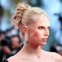 Alex Consani, con capelli biondi raccolti e un orecchino pendente con smeraldo, posa con sguardo intenso.