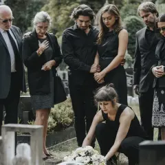 Famiglia in lutto, vestiti di nero per un funerale. Una donna depone fiori sulla tomba.