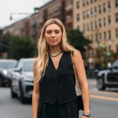 Donna con capelli biondi indossa un elegante gilet doppiopetto a righe, collana turchese e borsa a tracolla dorata, in strada.