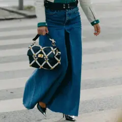 Un outfit gonna jeans lunga con borsa a tracolla trapuntata e tacchi lucidi, cammina su un attraversamento pedonale.