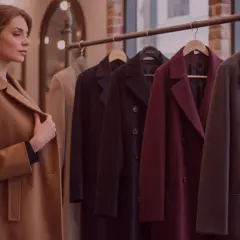 Donna osserva diversi tipi di cappotto in negozio: un modello cammello, nero, bordeaux e grigio scuro.