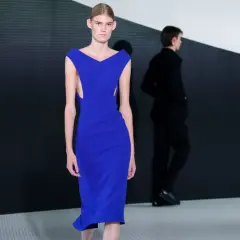 Modella con abito blu elettrico, un'opera di Simone Bellotti, sfila su una passerella minimalista.