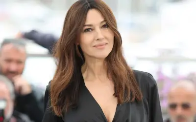 Monica Bellucci, icona di bellezza degli anni '90, con lunghi capelli castani e un abito scollato nero.
