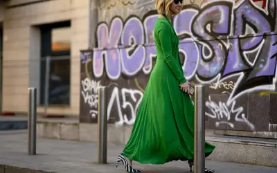 Donna con vestito lungo elegante verde smeraldo e scarpe zebrate, cammina con passo deciso davanti a un muro con graffiti.