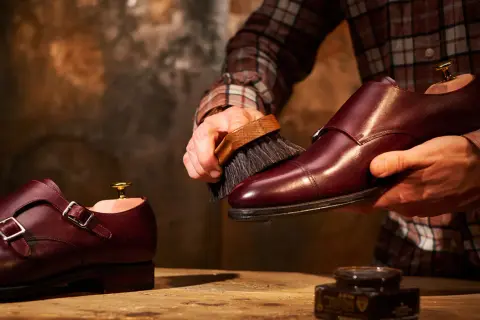Un uomo lucida scarpe in pelle bordeaux con una spazzola, un rituale per mantenerle splendenti.