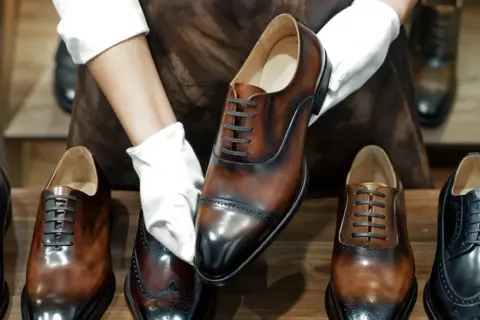 Mani guantate presentano una scarpa stringata marrone lucida, con la linguetta scarpa ben visibile. Altre scarpe eleganti in esposizione.