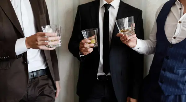 Uomini eleganti con bicchieri di whisky, perfetti per un dress code cocktail.