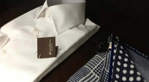 Camicia bianca da uomo con abbottonatura maschile impeccabile, accanto a un fazzoletto da taschino a pois e a quadretti.