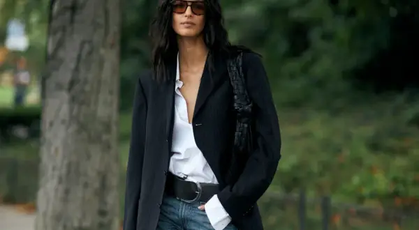 Donna con blazer gessato, camicia bianca sbottonata e jeans. Un look chic e casual.