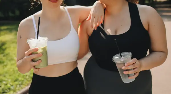 Due amiche con fianchi a violino si godono una bevanda fresca dopo l'allenamento, una con un matcha, l'altra con acqua.