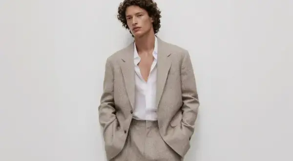 Uomo con giacca beige e camicia bianca sbottonata: un'idea di cosa mettere sotto la giacca uomo per un look casual-chic.