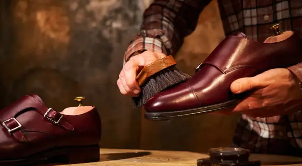 Un uomo lucida scarpe in pelle bordeaux con una spazzola, un rituale per mantenerle splendenti.